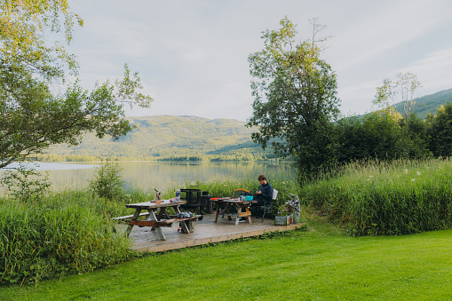 Side View of a male enjoying summer by the lake cooking pasta and having happy time with a dog in Nordland county, Northern Norway