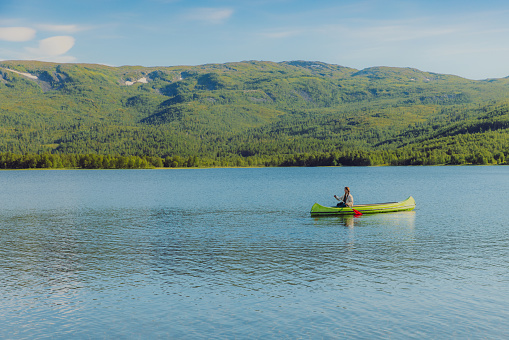 Side view of a female canoeing in the lake with view of green forest in Nordland county, Northern Norway