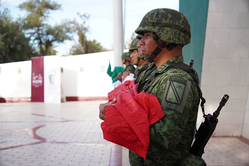 los mochis, Mexico – February 24, 2023: A group of military personnel in full camouflage attire stand in formation, proudly displaying the flag of Mexico