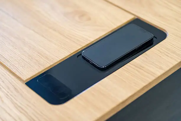Photo of Stylish wooden table with built-in wireless charger office table. Wireless charger for mobile phones, headphones and tablets. Wireless built-in charging station in the office