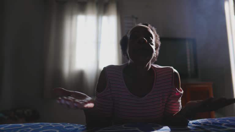 One Religious Black Senior Woman Praying in Silence kneeling by bedside in quiet Spiritual Meditation, hands clenched worhshiping GOD