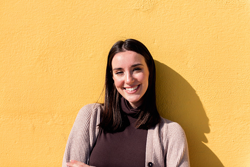 portrait of a young woman smiling happy looking at camera leaning in a yellow wall, concept of youth and lifestyle, copy space for text