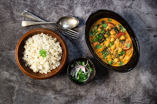 Chickpea curry with spinach has brown rice on black stale background, top view, healthy vegan food concept.