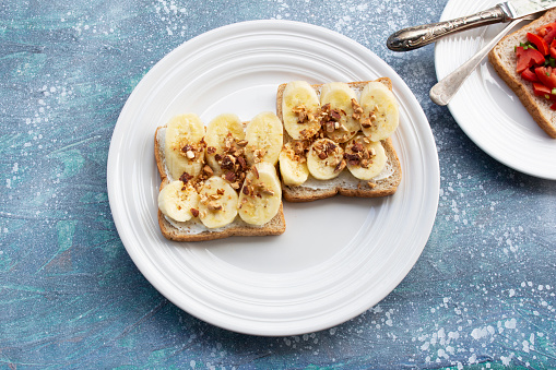 Sandwich open has banana cream cheese almonds and tomato on wood background, top view, copy space, breakfast food concept.