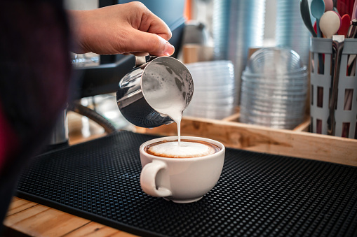 barista pouring milk into coffee making cappuccino. Professional barista preparing coffee on the counter.