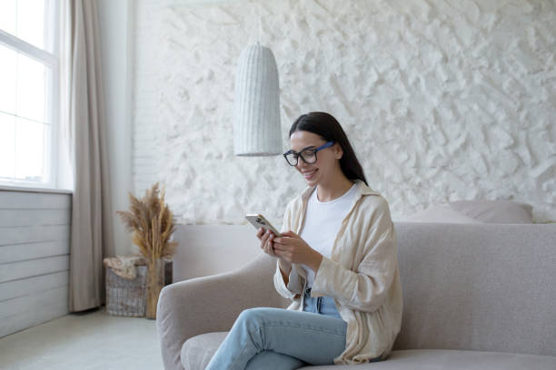istock Young smiling woman sitting on sofa at home and using mobile phone. Writes messages, chats, online shopping, reads news 1501137005