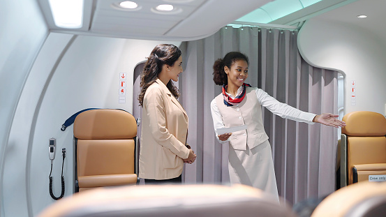 Young women flight attendant, stewardess in uniform standing in the airplane entrance smiled friendly and checking passenger's boarding pass and welcoming to the flight. Airline transportation