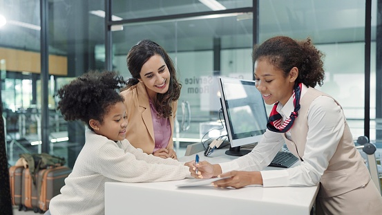 American african women airline ground staff worker giving boarding pass or ticket to passenger woman mother and little daughter at airport check in counter. Family travelling concept