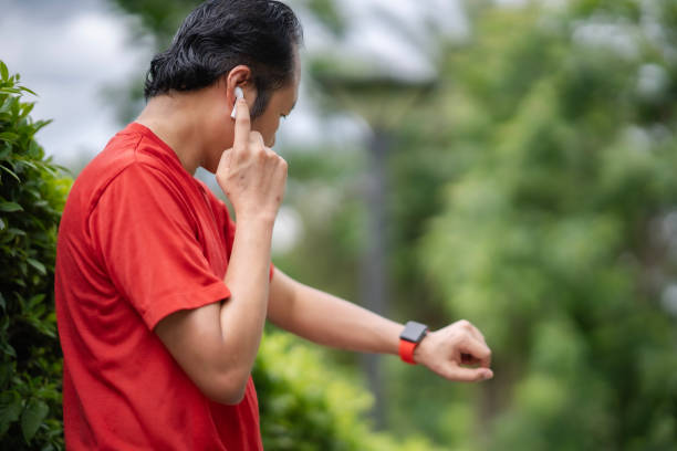 istock Side of Middle age man standing at park, touching white Bluetooth earphone and looking red band smartwatch. 1501146952