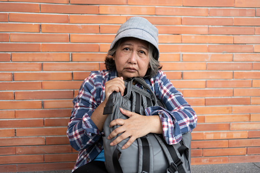 Poor tired stressed depressed elderly Asian woman homeless sitting on the street in the shadow of the building and begging for help and money, Elderly Asian woman abandoned concept
