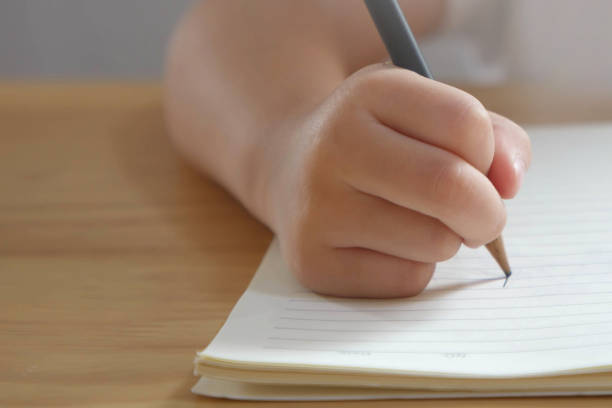 istock Kid hand writing with pencil in a book on wooden table 1501157416