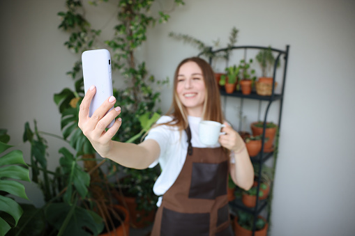 Smiling woman florist taking selfie with her plants for publishing in social media in florar studio