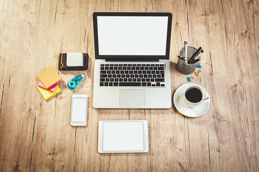 Top view of a modern office business table with coffee, laptop, digital tablet and smartphone with blank screens.