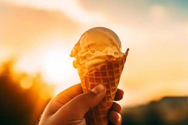 An Ai-generated illustration of a person's hand holding a slightly-melted delicious vanilla ice cream in a cone