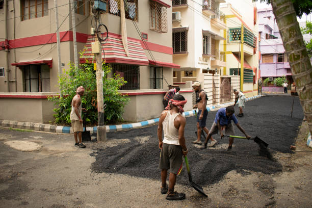 khanpur road, kolkata, west bengal, india - june 24, 2023 : road construction workers manually spreading and stretching bitumen mixture dumped on the road for construction