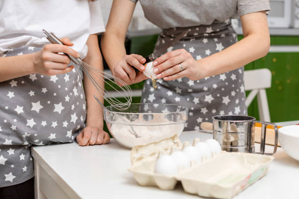 as mãos de uma mulher quebram um ovo em uma tigela de farinha em casa. o processo de fazer massa de biscoito. - cake making mixing eggs - fotografias e filmes do acervo