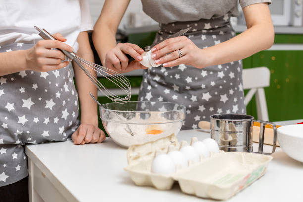 руки женщины разбивают яйцо в миску с мукой дома. процесс приготовления теста для печенья. - cake making mixing eggs стоковые фото и изображения
