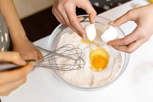 as mãos de uma mulher quebram um ovo em uma tigela de farinha em casa. o processo de fazer massa de biscoito. - cake making mixing eggs - fotografias e filmes do acervo