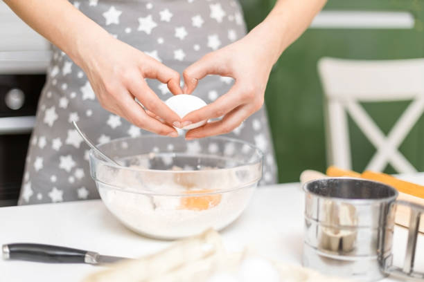 as mãos de uma mulher quebram um ovo em uma tigela de farinha em casa. o processo de fazer massa de biscoito. - cake making mixing eggs - fotografias e filmes do acervo