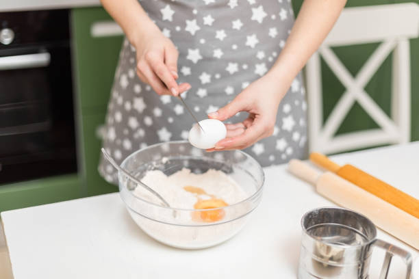 руки женщины разбивают яйцо в миску с мукой дома. процесс приготовления теста для печенья. - cake making mixing eggs стоковые фото и изображения