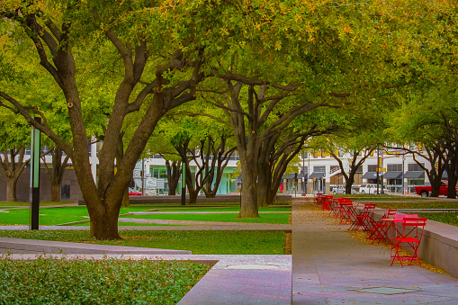 A beautiful park in downtown Fort Worth, Texas with red outdoor seating and live oak trees