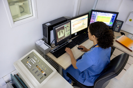 Latin American female radiologist in the control room taking an x-ray image at the hospital - healthcare and medicine concepts
