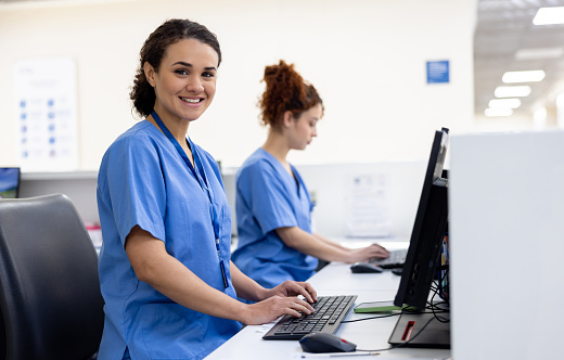 Happy receptionists working at a hospital using computers and looking at the camera smiling - healthcare workers concepts