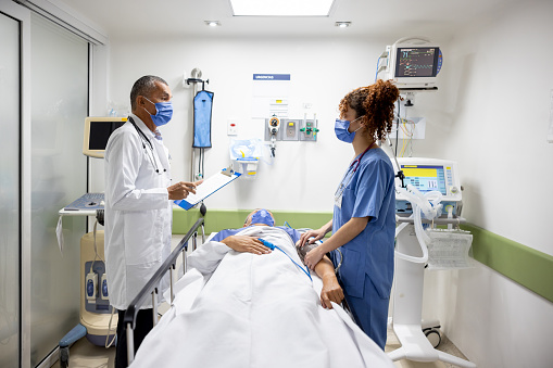 Latin American doctor and nurse talking while treating a patient in the ICU at the hospital - healthcare and medicine concepts