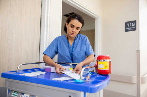 Latin American nurse working at the hospital dispensing medicine in the rooms - healthcare and medicine concepts