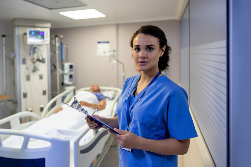 Portrait of a Latin American nurse working at the ICU and checking on a patient - healthcare and medicine concepts