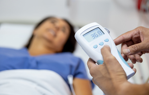 Close-up on a nurse taking the temperature of a patient at the hospital - healthcare and medicine concepts