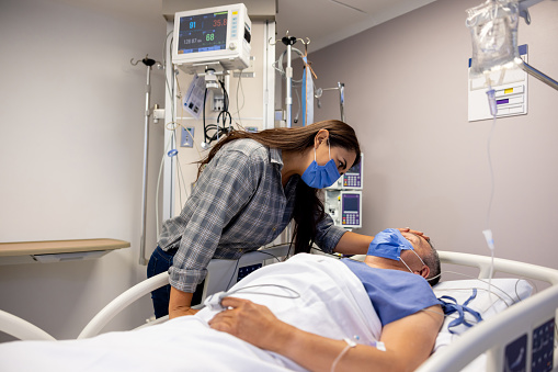 Latin American woman wearing a face mask while visiting a patient at the hospital in the ICU - healthcare and medicine concepts