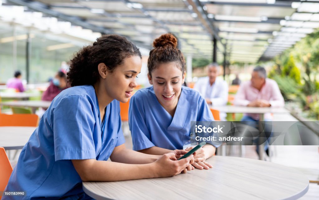Nurses taking a break and looking at social media at the cafeteria Nurses taking a break from work at the hospital and looking at social media on a cell phone at the cafeteria Nurse Stock Photo
