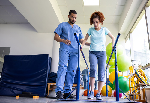 Woman recovering from an injury and walking on bars with the assistance of her physical therapist