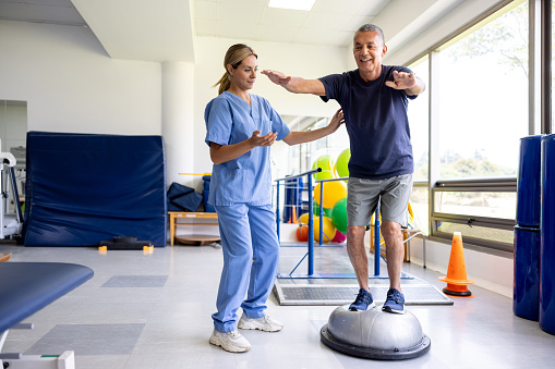 Mature man doing physical therapy exercises using a balance ball with the guidance of his therapist
