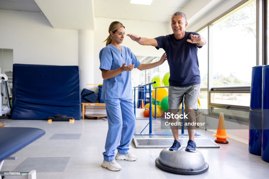 Man doing physical therapy exercises using a balance ball Mature man doing physical therapy exercises using a balance ball with the guidance of his therapist Physical Therapy Stock Photo