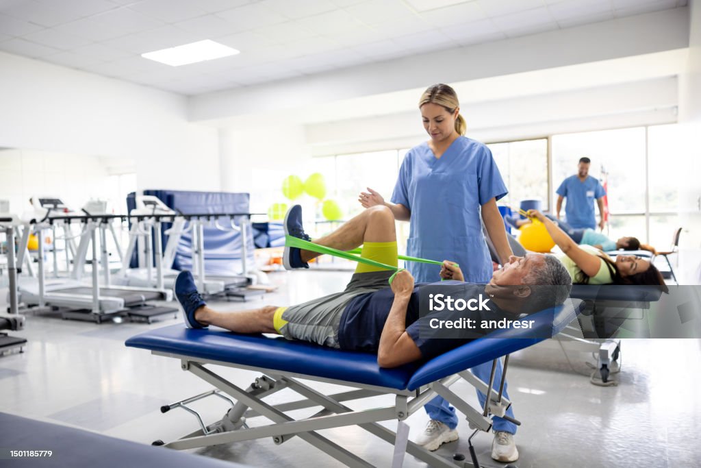 Man doing physical therapy exercises using a stretch band Mature Latin American man doing physical therapy exercises using a stretch band with the assistance of his therapist Physical Therapy Stock Photo