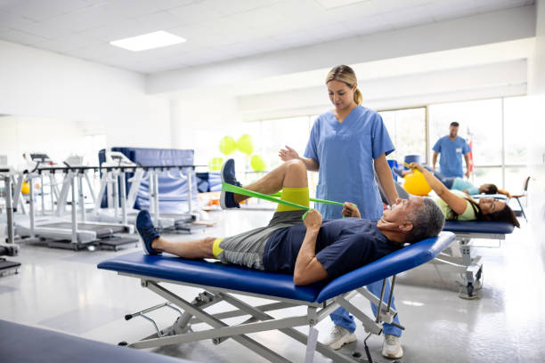 Man doing physical therapy exercises using a stretch band Mature Latin American man doing physical therapy exercises using a stretch band with the assistance of his therapist physiotherapy stock pictures, royalty-free photos & images