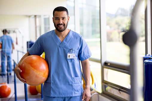 Portrait of a Latin American physical therapist working at a rehabilitation center and holding a fitness ball while looking at the camera smiling