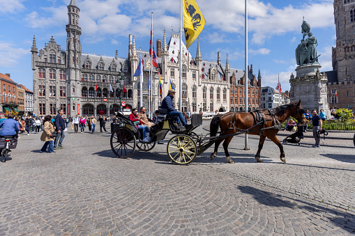 Bruges, Belgium - May 19, 2023: Carriage on the Main Square (Grote Markt), with guests riding around the market. Historic buildings in the background