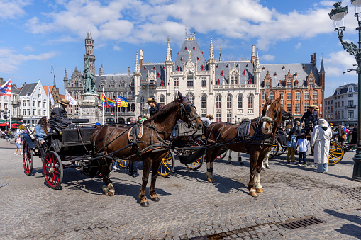 Bruges, Belgium - May 19, 2023: Horse-drawn carriage at Main Market Square (Grote Markt), waiting for visitors who want to ride around the square. Historic buildings in the background
