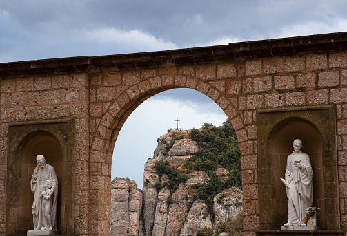 Saint Michaels Cross, sitting on top of Montserrat, through the archway and sculptures at Monsterrat Ministery, Barcelona, Spain.