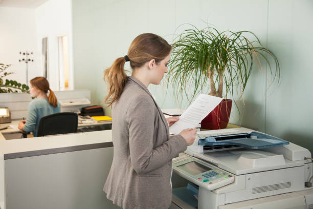 Young businesswoman talking on cell phone by the copy machine in the office. The view is through glass. Copy space.