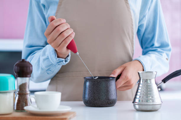 Woman using a frother for making aromatic coffee at home