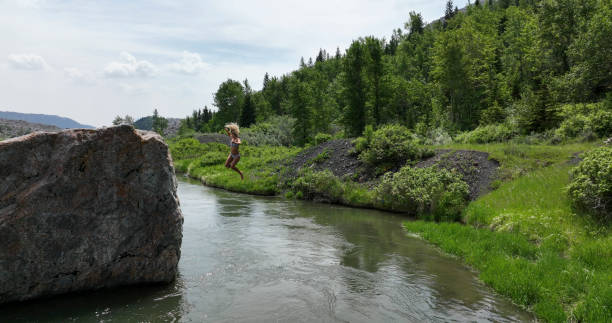 istock Young woman jumps off rock in river 1501210729