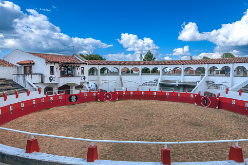 Guatavita, Colombia - January 21, 2017: The small, mock bullring in the Colombian town of Guatavita on the Andes Mountains in South America. The place is a tourist attraction and there are no entrance tickets required. Photography is freely allowed inside the entire facility. The location is often the scene of events and exhibitions. In the background are the Andes Mountains. The altitude of the town is about 8,790 feet above mean sea level. Photo shot in the afternoon sunlight; horizontal format. No people. Copy Space.