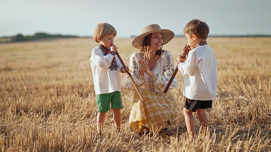 Boys playing on wooden flutes - sopilka. Ukrainian mother with children sons in wheat field. Woman in embroidery vyshyvanka. Ukraine, traditional music instrument, melody, song. High quality photo