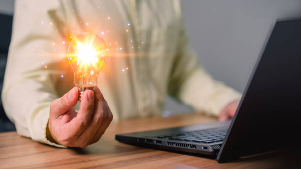 istock Man holding a light bulb while working on a computer laptop to think and generate new ideas through technological innovation and creativity. Idea inspired by online technology and innovation. 1501219327
