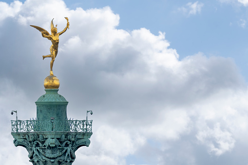 Close up detail of gilded winged Mercury atop the Bastille Column in Paris France with copy space on a blue sky cloud background. Concept victory, liberty