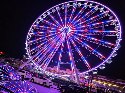 A brightly illuminated Ferris Wheel at night in St. Louis, MO with its light reflecting on a car.